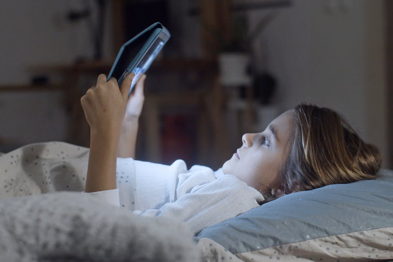 Photo of a girl lying-on-bed-while-holding-a-tablet